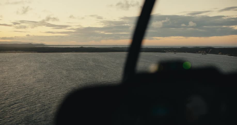 Aerial view from inside a helicopter flying over a coastal landscape during sunset