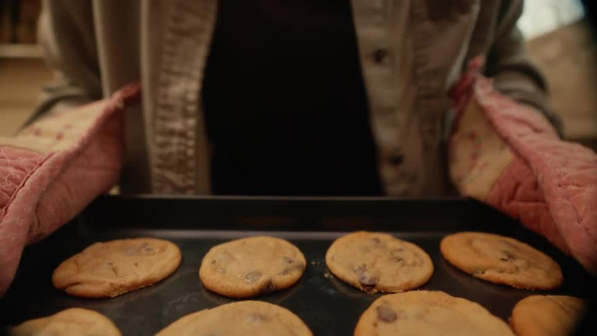 Point of view taking freshly baked chocolate chip cookies out of oven then setting on counter