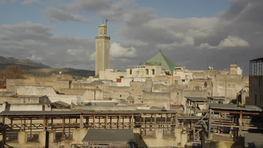 Old cityscape with a tall minaret and greenroofed mosque under dramatic clouds