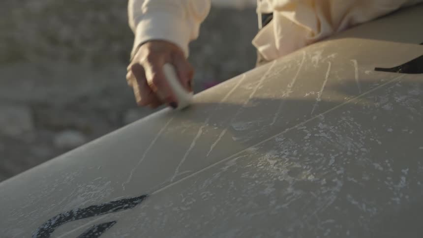 Surfer scoring top of surfboard with wax at the beach