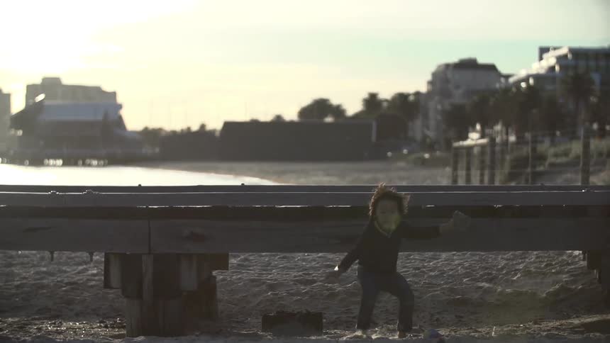 Child jumping off of a dock onto the sand on a beach