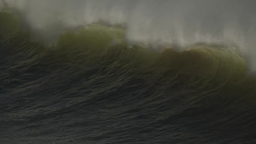 A surfer dives into the water ahead of a big wave