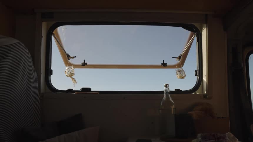 A window with the glass open to the sky which is blue and in front of it a table with a glass bottle filled with white liquid