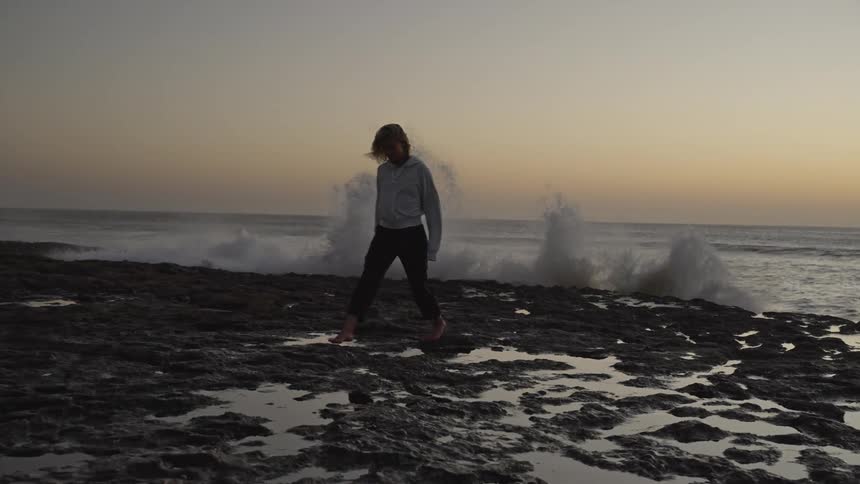 A young woman walks along an ocean shore at sunrise