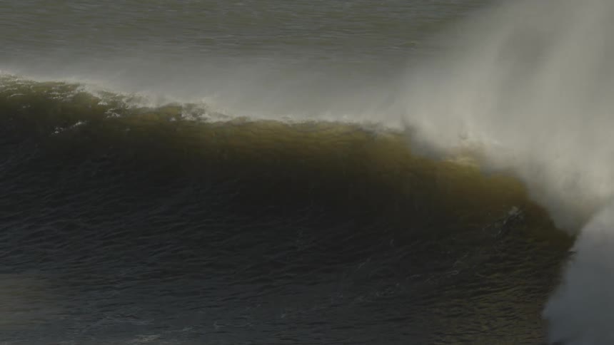 A surfer rides the crest of a powerful wave as another surfer waits in the water below