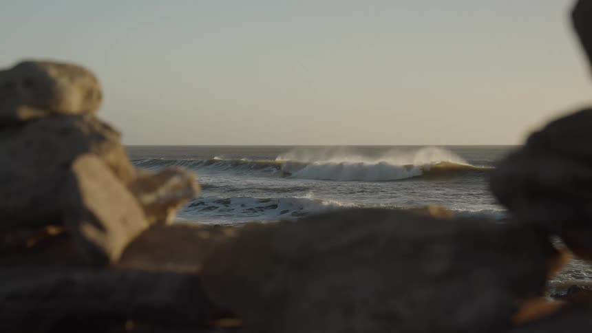 Rocks and a beach in the background with waves and a clear sky