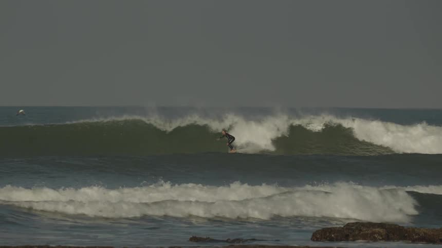 A woman surfing a wave in the ocean with other people lying on their surfboards further behind