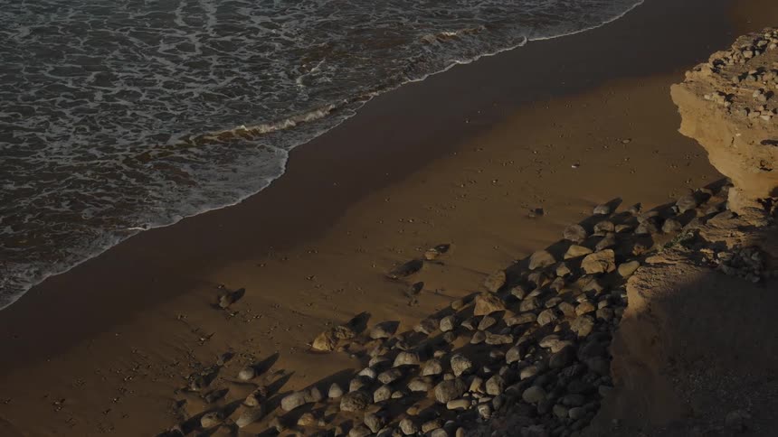 Cliff overlooking rocks on the beach as waves roll into shore