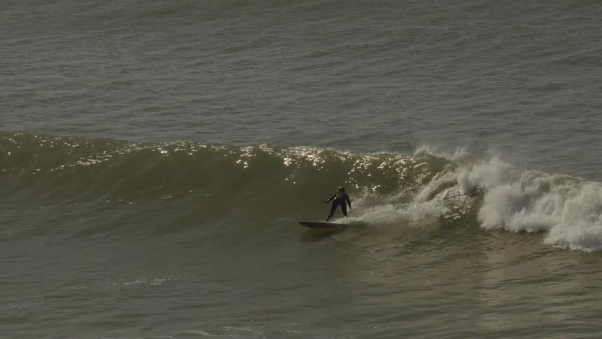 A surfer rides a breaking wave while others wait in the background