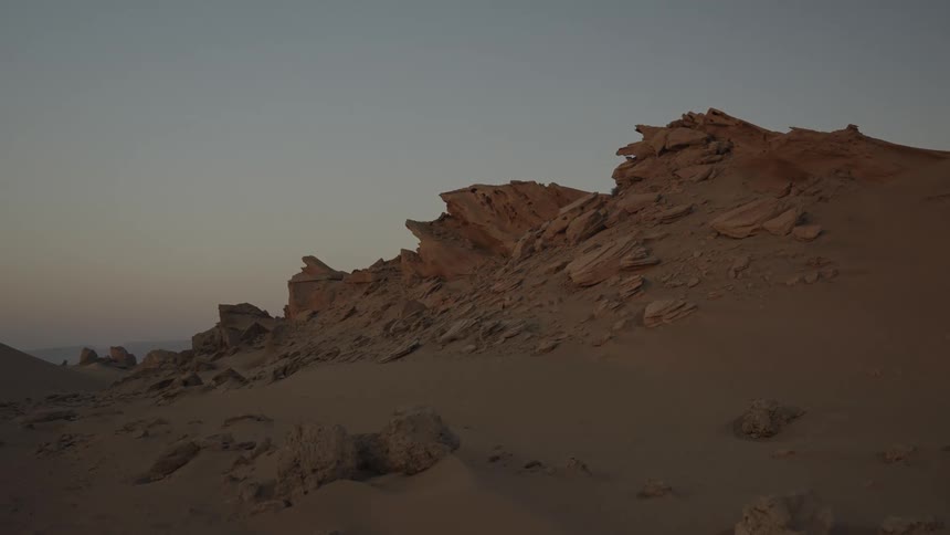 Jagged winderoded rock formations rise from a sandy landscape under a pale sky