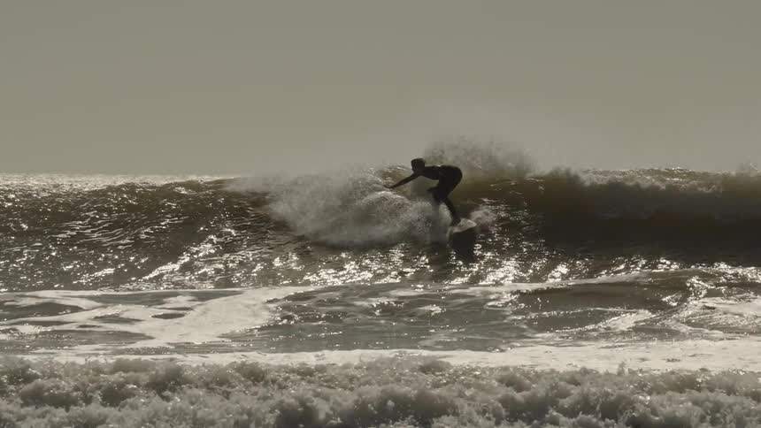A surfer riding an ocean wave while other people swim at sunset