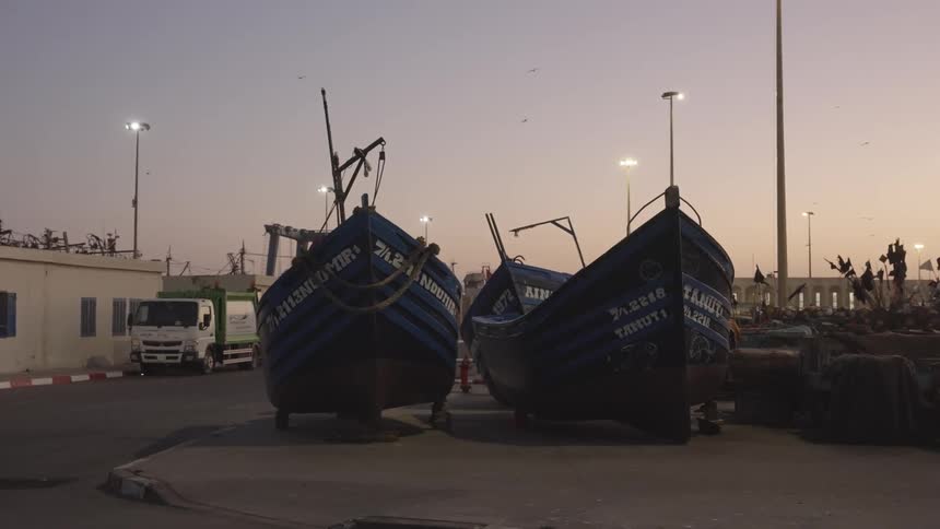 Two wooden fishing boats on a city sidewalk in a violet sky sunrise with birds flying