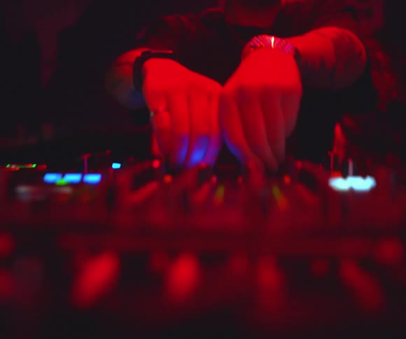 The hands of a dj playing on decks in a red lit environment