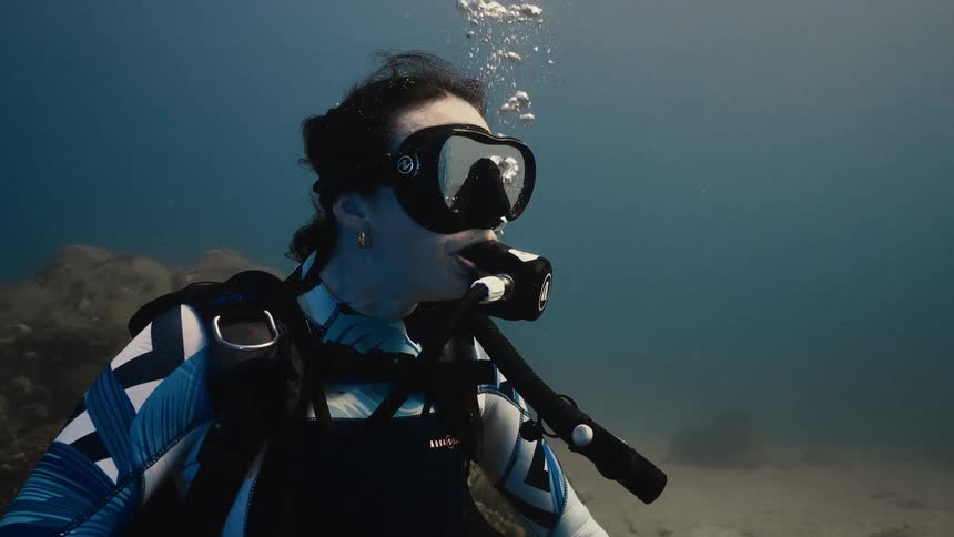 A female scuba diver is seen underwater breathing through her regulator while observing the surroundings