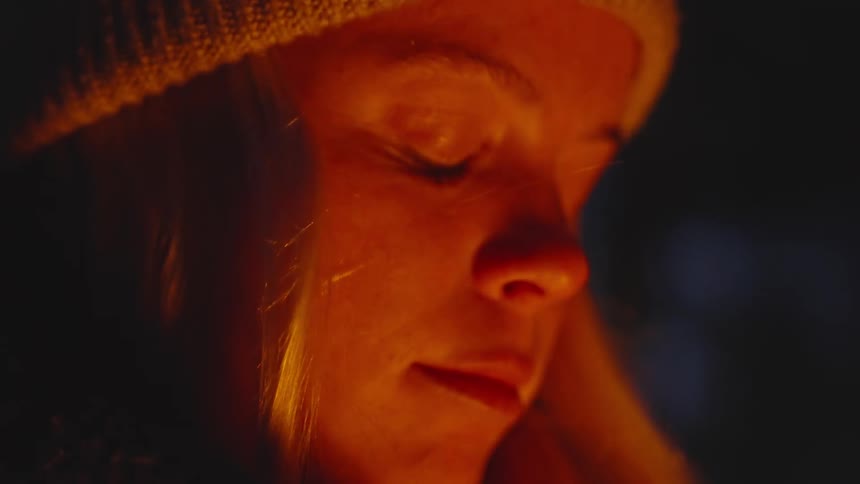 The light from the campfire flickers on the womans face