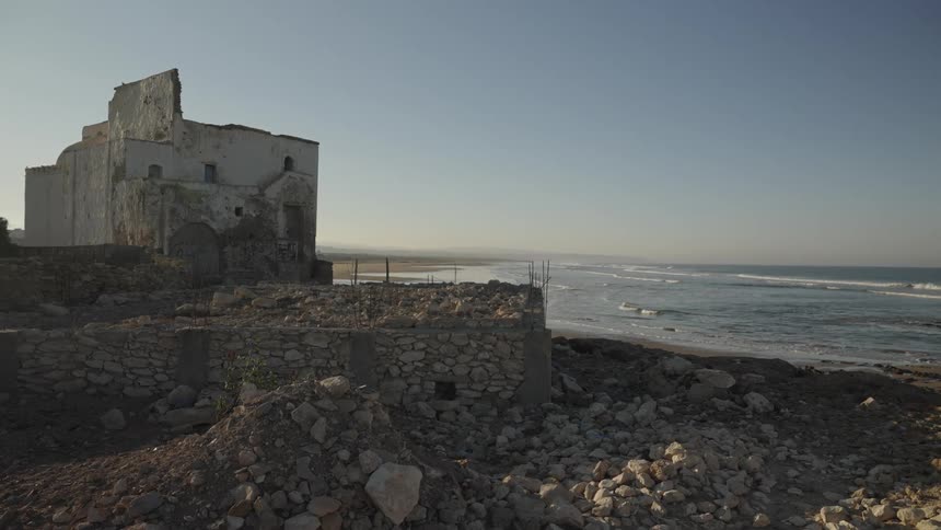 Old stone building by a rocky shore with waves and a clear sky