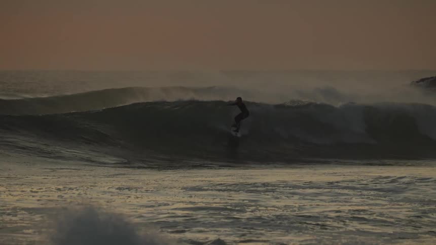 Surfers ride surfboards across choppy ocean waters under a red tinted sky