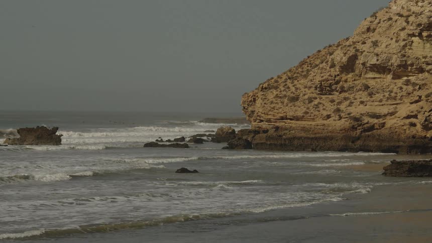 Waves roll into shore among rocks at the promontory under a hazy sky
