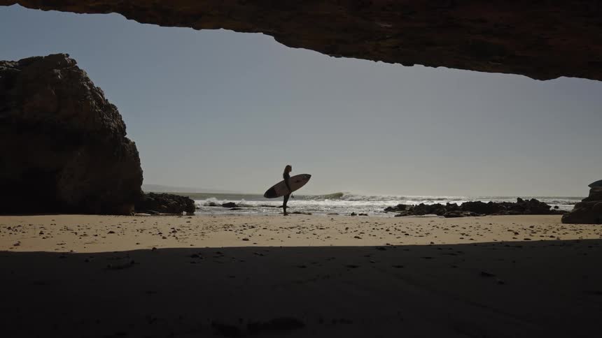A lady holding a surfboard stands still at the beach on a sunny day