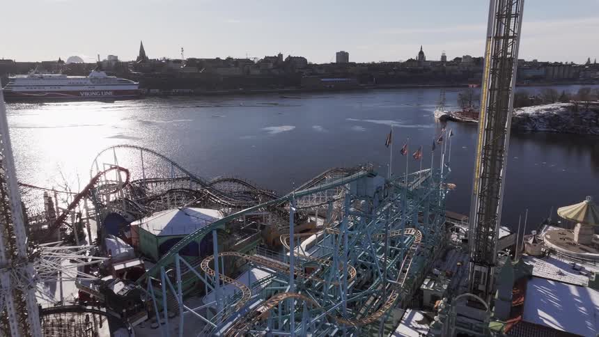 Aerial view of a snowy amusement park with roller coasters by the water city skyline in the background