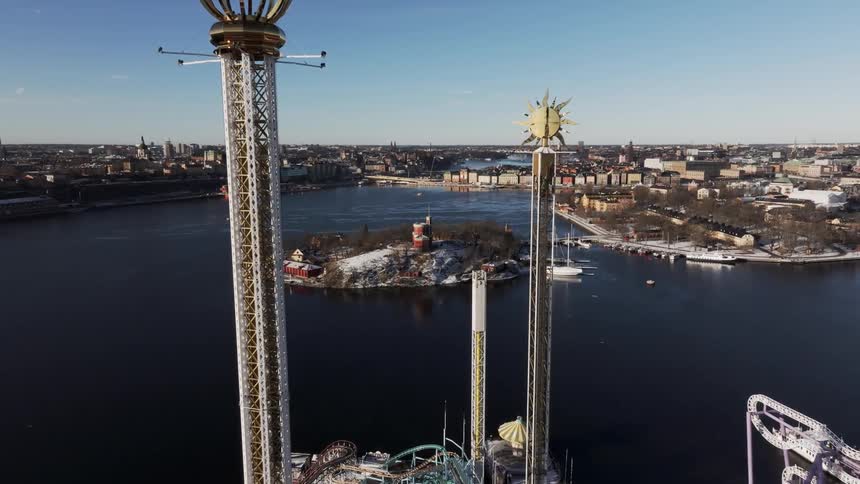 Aerial view of a waterfront amusement park in winter with tall rides roller coasters and a city skyline in the background