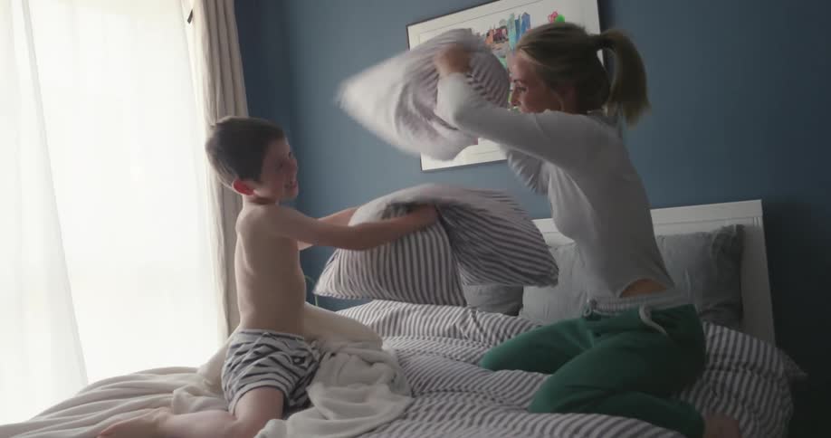 Mother and son laughing having a pillow fight on the bed in the morning