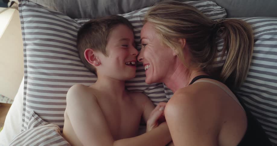 A mother and son laugh and talk in bed
