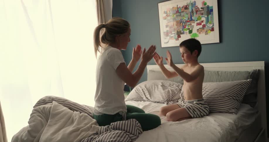 Mother and son sitting on the bed playing patty cakes in the morning