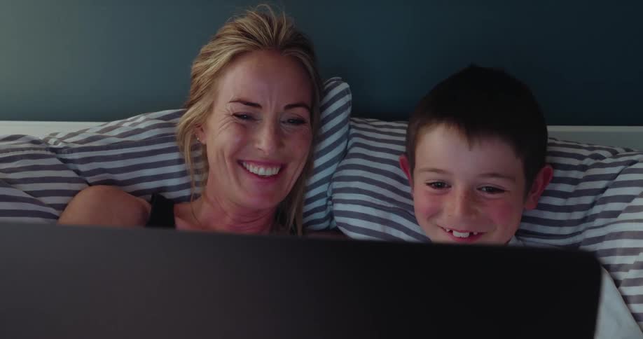 Mother and son laying in bed laughing watching a show from laptop