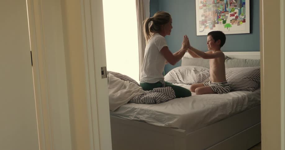 Mother and son plays and laughs on the bed at daytime