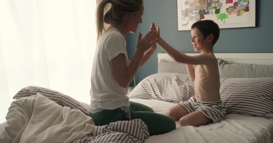Mother and son sitting on the bed playing patty cakes in the morning