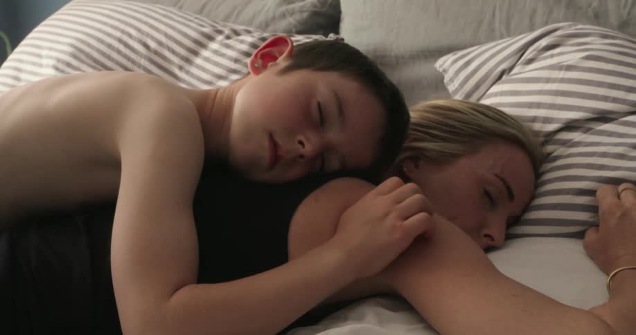 Boy sleeping on top of mother in bed