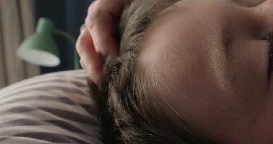 A closeup of a child peacefully sleeping in bed with a hand gently touching their hair