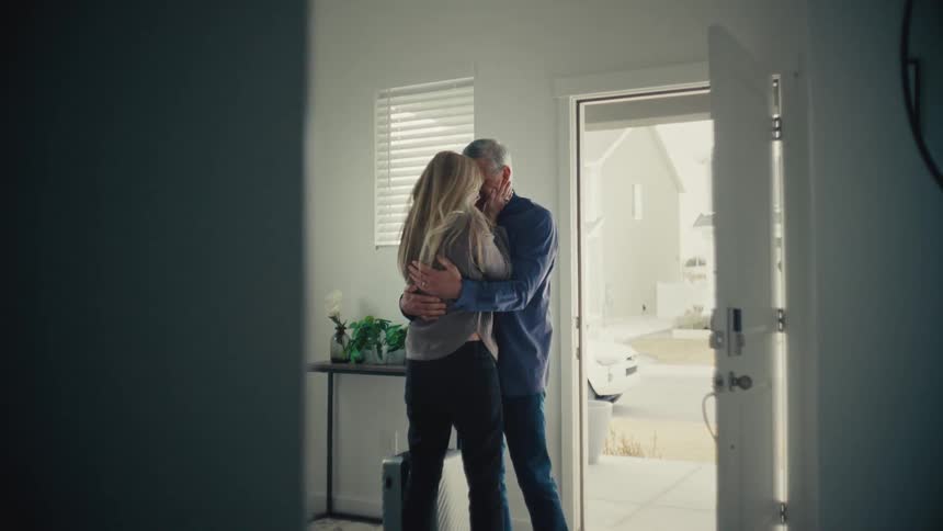 A man and woman share a warm embrace at the front door hinting at a heartfelt reunion in a cozy suburban setting