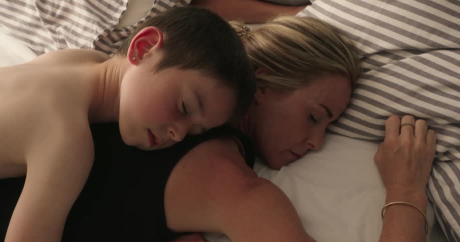 A tender moment as a young boy sleeps peacefully on top of a woman likely his mother both resting in bed