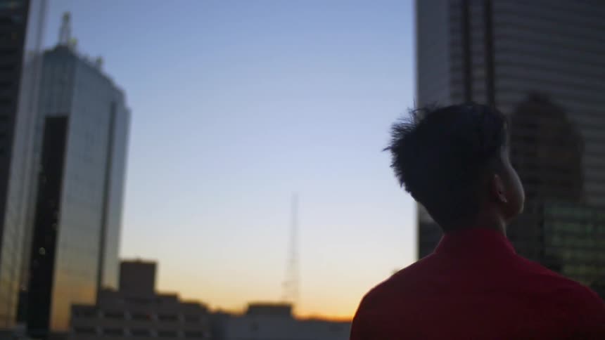 Young man looks up at tall buildings at sunset
