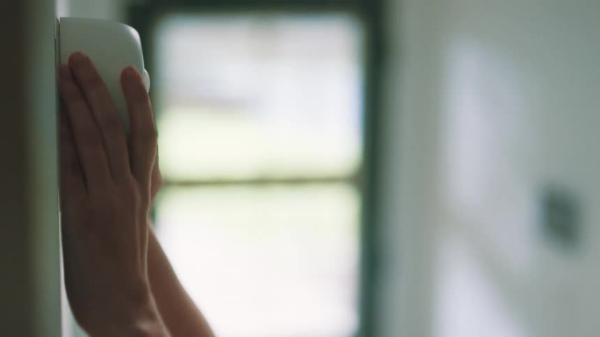 A woman reaches over and touches the device on the wall