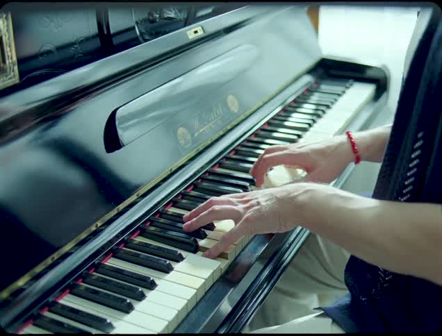A person plays an upright piano in a softly lit room with focus on their hands and upper body