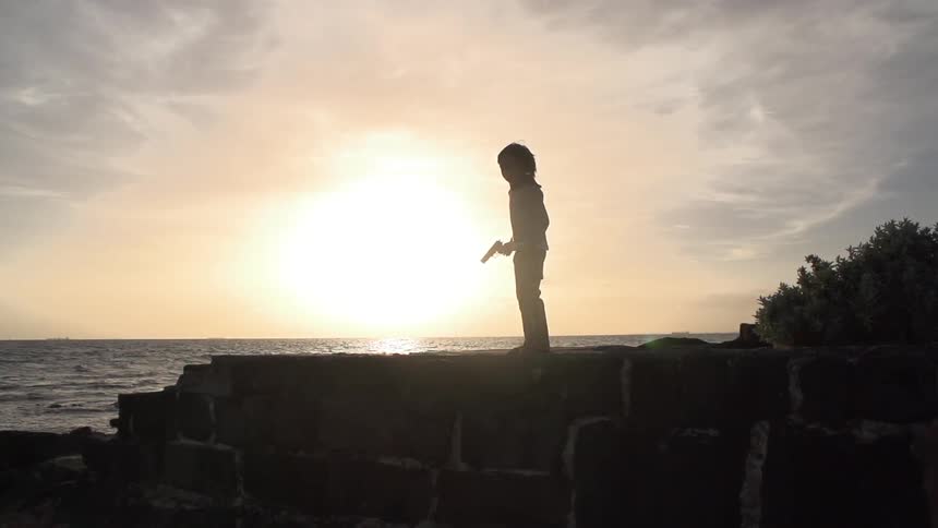 Child holding a gun on a wall at sunrise