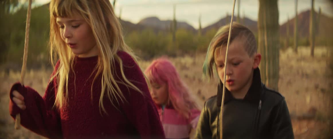 Three children are walking in a desert on a mostly cloudy day