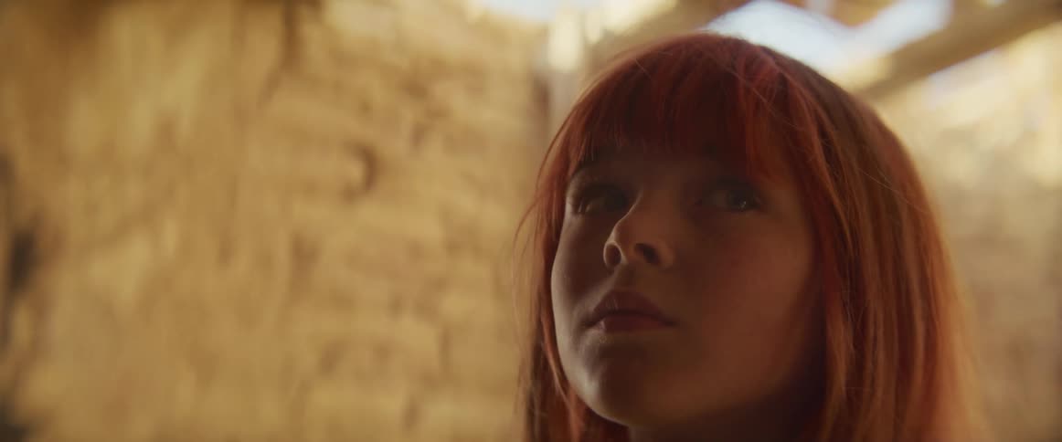 A redhaired girl explores a sunlit stone ruin her face softly lit by beams from the broken ceiling