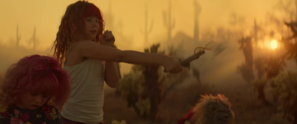 A group of girls is practicing with slingshots in a desertlike landscape as the sun sets