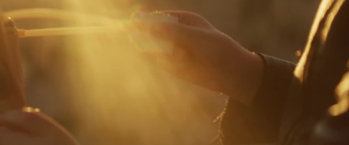Hands pull back the elastic band of a wooden slingshot ready to release a projectile in the warm golden sunlight of a desert at sunset