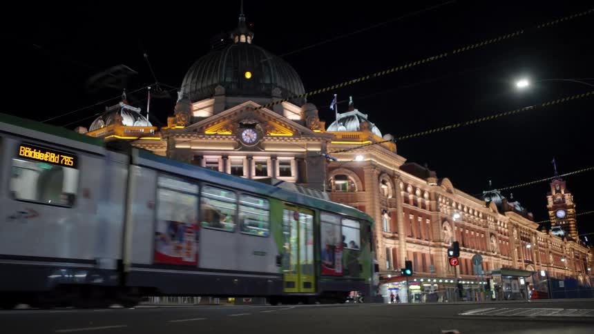 At night in melbourne australia flinders street station glows with its yellow facade as a tram approaches on the city street