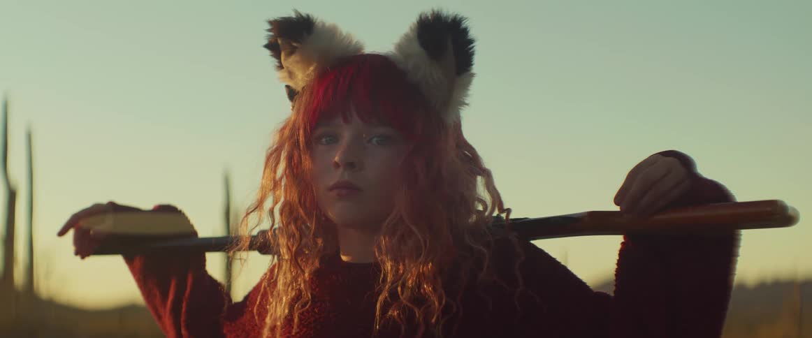 A girl wearing a headband with animal ears resting a rifle on her back