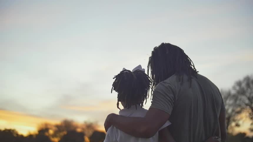 A man and girl hug at sunset