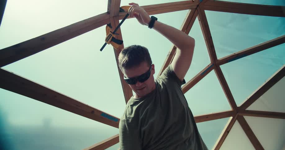 Man building a multi paneled dome attaches clamps to a pair of joints on a sunny day