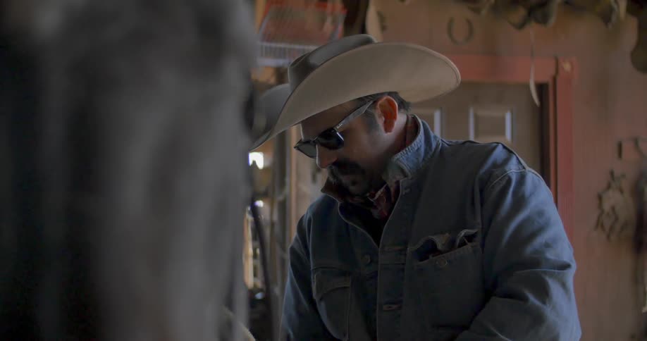 A man in a cowboy hat tightens a saddle