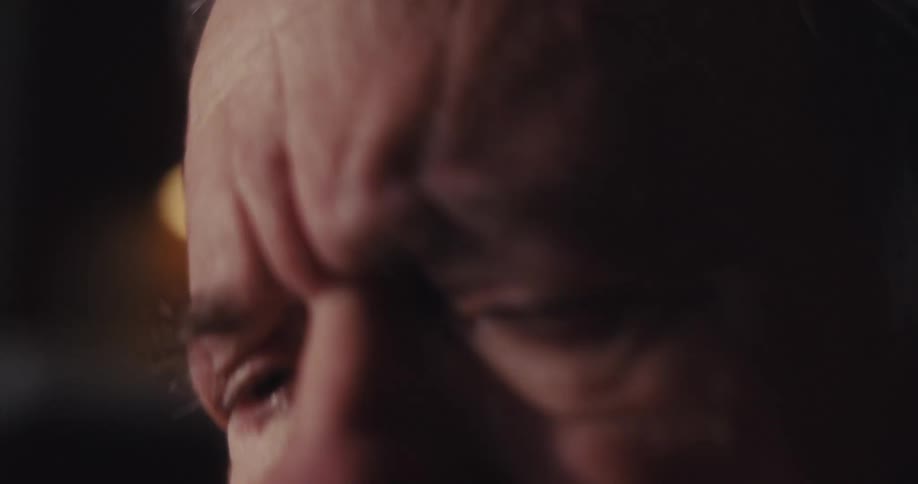 Elderly man sitting at a table with a computer looks around while thinking