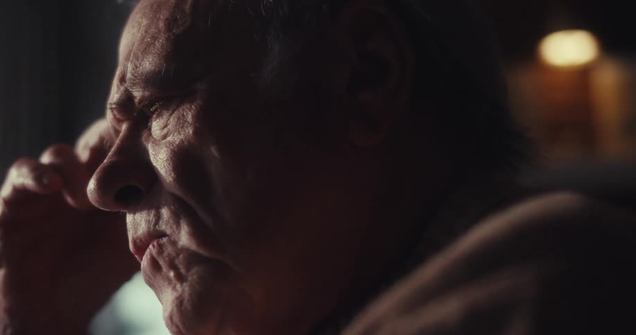 Elderly man sitting while watching something at home frowns in thought